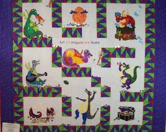May include: A colorful quilt with a purple background and a green and white maze pattern. The quilt features various dragons with different colors and designs. The text "Not All Dragons Are Scary" is written in the center of the quilt.