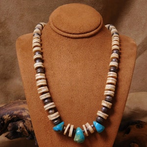 May include: A necklace made of white and silver beads with turquoise accents. The necklace is on a brown mannequin.