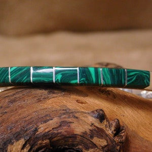 May include: A silver bracelet with a green malachite inlay. The bracelet is made of sterling silver and features a smooth, polished finish.