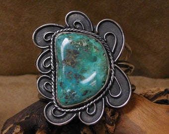 May include: A silver bracelet with a large turquoise stone set in a decorative swirl design.