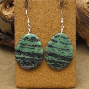 May include: A pair of silver dangle earrings with green and black oval-shaped stones. The stones have a marbled pattern.