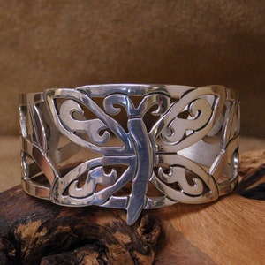 May include: A silver bracelet with a cutout butterfly design. The bracelet is made of metal and has a polished finish.