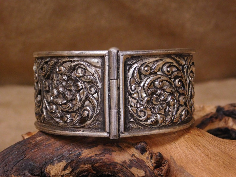 May include: A silver bracelet with intricate floral designs. The bracelet is hinged and opens to fit the wrist.
