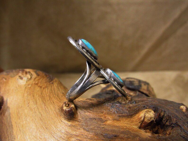 May include: A silver ring with two turquoise stones set in a decorative design. The ring is on a wooden surface.