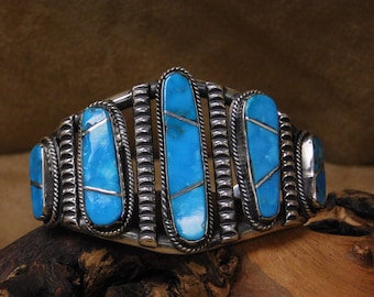 May include: A silver bracelet with turquoise stones set in a geometric pattern. The bracelet is made of sterling silver and features a unique design.