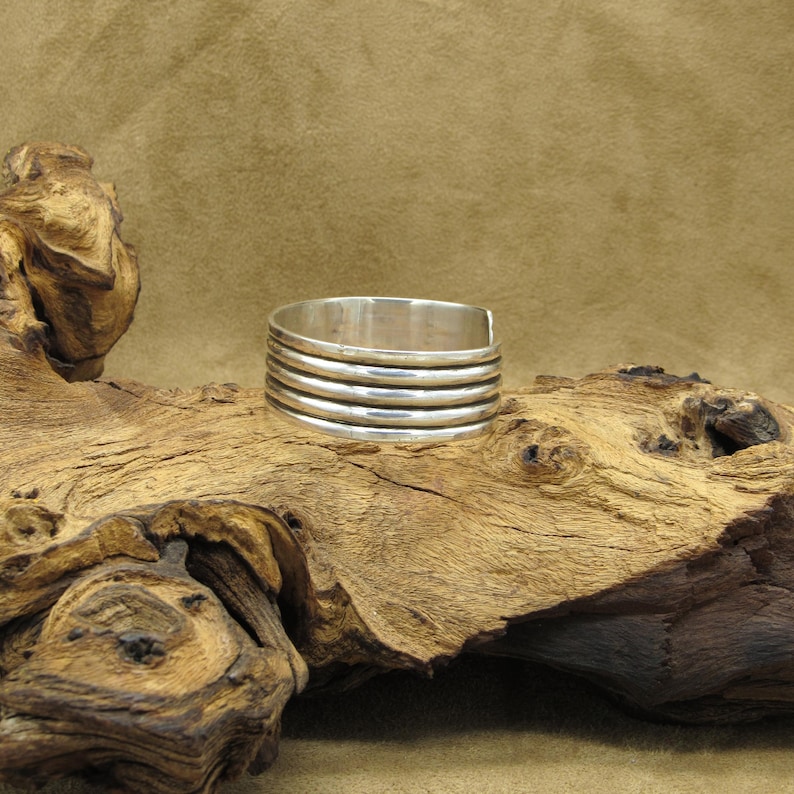 May include: A silver cuff bracelet with a stacked design. The bracelet is made of multiple bands of silver that are stacked on top of each other.