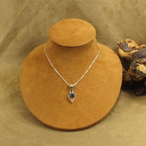 May include: A silver necklace with a teardrop-shaped pendant. The pendant features a mosaic design with orange, green, blue, and purple sections. The necklace is displayed on a brown jewelry bust.