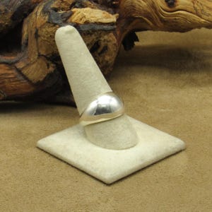 Peut inclure: Une bague en argent poli avec un design arrondi et bomb&eacute;. La bague est pr&eacute;sent&eacute;e sur un pr&eacute;sentoir &agrave; bagues beige clair, mettant en valeur sa surface lisse et r&eacute;fl&eacute;chissante. Son style simple mais &eacute;l&eacute;gant en fait un accessoire polyvalent.