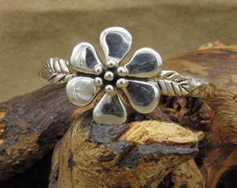 May include: A silver flower cuff bracelet with a detailed leaf design. The flower has five petals and a center with small, round accents.