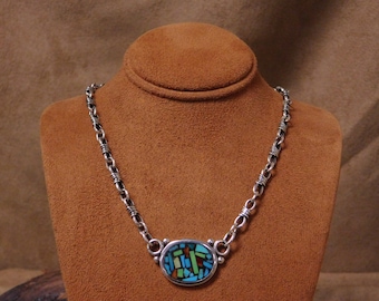 May include: A silver chain necklace with a round pendant featuring a mosaic of turquoise, red, green, and brown stones.