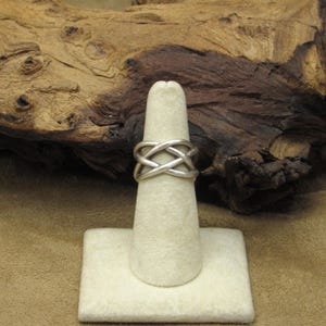 May include: A silver ring with a woven design. The ring is displayed on a white ring stand.