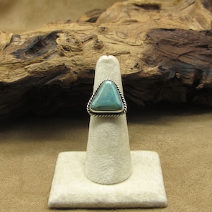 May include: A silver ring with a triangular turquoise stone set in a silver bezel. The ring is on a white display stand.