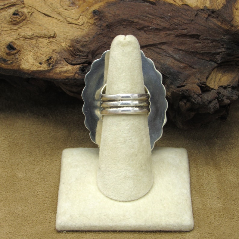 May include: A silver ring with a scalloped edge and a triple band design. The ring is on a white ring display stand.