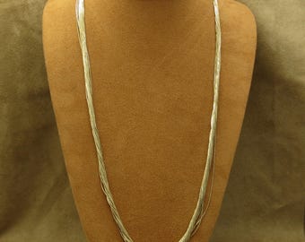 May include: A multi-strand silver necklace displayed on a brown jewelry bust. The necklace features numerous thin, delicate strands that cascade down, creating a flowing, elegant look. The silver color provides a bright contrast against the bust.