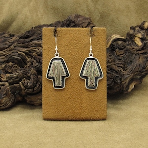 May include: A pair of silver earrings with a unique design. Each earring features a black outline with a stylized shape filled with a pattern of green, red, and tan lines. The earrings hang from silver hooks.