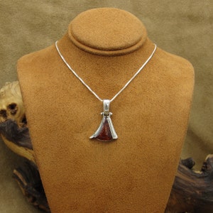 May include: A silver necklace with a pendant featuring a reddish-brown stone. The pendant has a unique, angular design with a silver frame. The necklace is displayed on a brown jewelry bust.