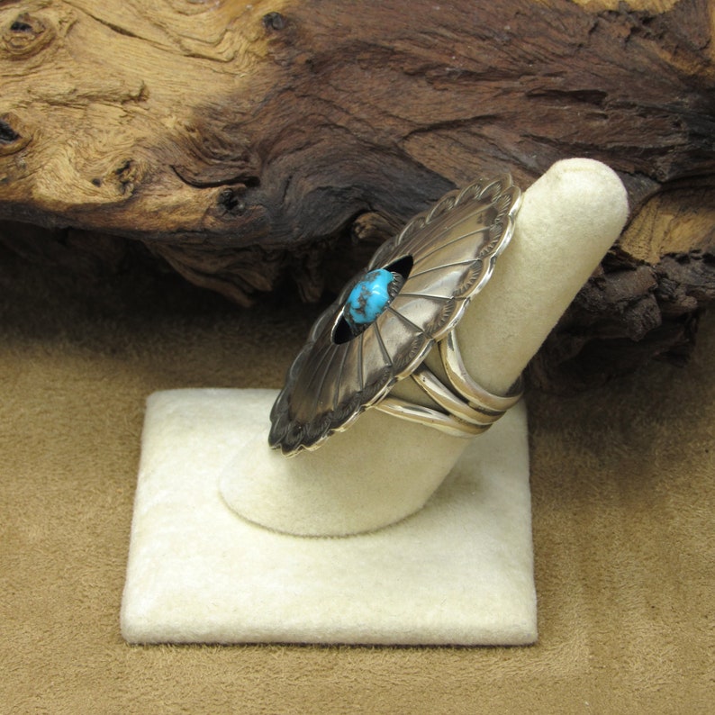 May include: A silver ring with a turquoise stone set in a circular design. The ring is on a white display stand.