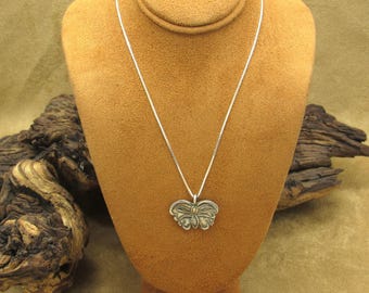 May include: A silver chain necklace with a silver butterfly pendant. The butterfly has a textured design and a small yellow gemstone in the center.