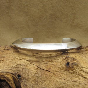 May include: A silver bracelet with a pointed, angular design. The bracelet is made of a smooth, polished metal and has a simple, minimalist style.