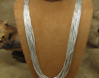 May include: A silver necklace made of multiple strands of small, round beads. The necklace is displayed on a brown mannequin.