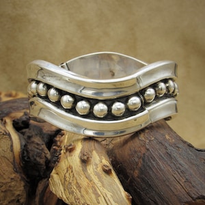 May include: A silver bracelet with a wavy design and a row of beads along the top and bottom.