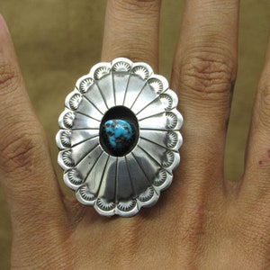 May include: A silver ring with a turquoise stone set in the center. The ring has a sunburst design with a scalloped edge.