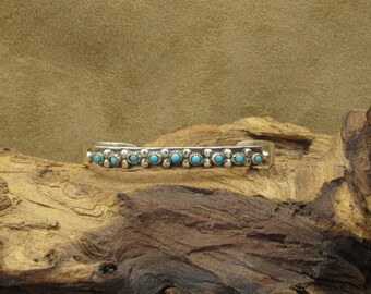 May include: A silver bracelet with a row of turquoise stones set in a floral design.
