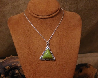 May include: A silver necklace with a triangular pendant. The pendant has a light green stone set in a decorative silver frame. The necklace is displayed on a brown bust.
