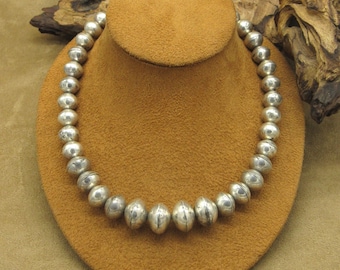 May include: A silver necklace with round beads. The beads are smooth and have a slightly textured surface. The necklace is on a brown velvet display stand.