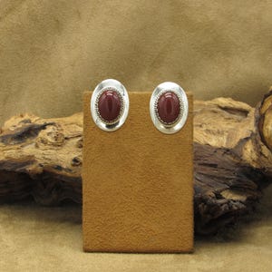 May include: A pair of silver earrings with red carnelian stones. The earrings are oval shaped and have a silver border.