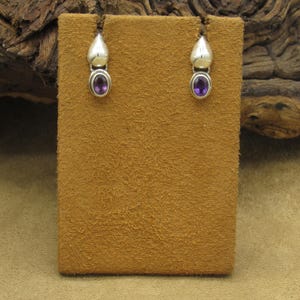 May include: A pair of sterling silver earrings with small purple amethyst stones. The earrings are teardrop shaped and have a smooth, polished finish.