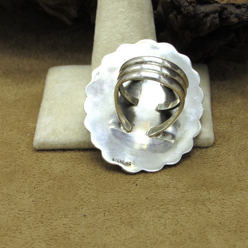 May include: A silver ring with a round, scalloped design. The ring is marked "STERLING" on the back.