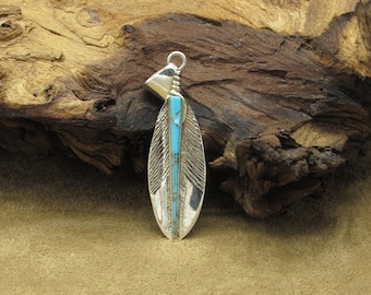 May include: A silver pendant in the shape of a feather with turquoise inlay. The pendant is on a wooden surface.