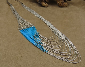 May include: A multi-strand silver necklace with turquoise beads. The necklace is made of many thin silver chains and has a cascading design of turquoise beads.