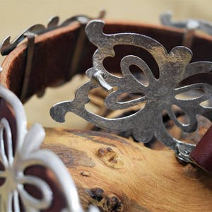 May include: A brown leather belt with a silver butterfly buckle. The buckle is detailed with intricate cutouts and has a decorative design.