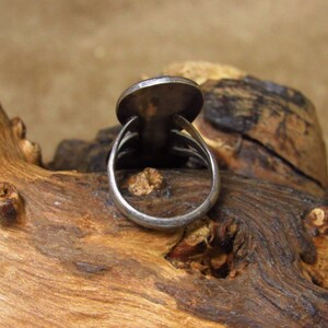 May include: A silver ring with a round, flat top. The ring is on a piece of wood.