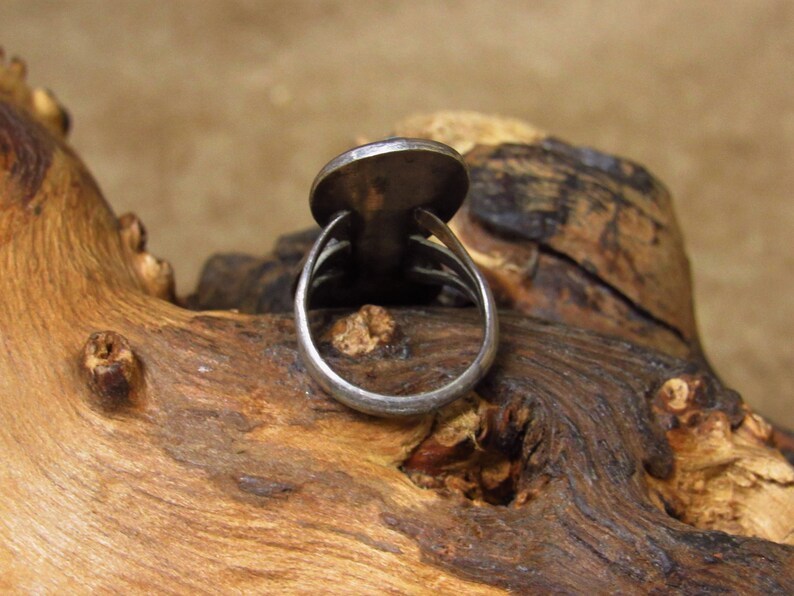 May include: A silver ring with a round, flat top. The ring is on a piece of wood.