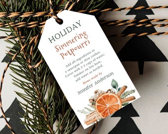 May include: A white gift tag with the words "HOLIDAY Simmering Potpourri" in green and orange. The tag includes instructions and a watercolor illustration of orange slices and cinnamon sticks. The tag is tied to a gift with twine and evergreen branches.