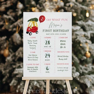 以下が含まれることがあります： 赤い車とクリスマスツリーが描かれた赤と緑のファーストバースデーの記念ポスター。ポスターには、子供の年齢、身長、体重、好きな食べ物、おもちゃ、本が記載されています。テキストには「Oh What Fun Mason's First Birthday May 16th, 2022 | 8:24PM」とあります。