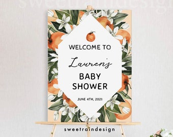 May include: Welcome to Lauren's Baby Shower sign with orange blossoms and greenery on a peach background. The date June 4th, 2021 is printed below the text.