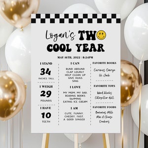May include: A black and white checkered sign with the text "Logan's TWO COOL YEAR" in a black and white font. The sign also includes details about Logan's age, height, weight, and favorite things. The sign is on a wooden easel.