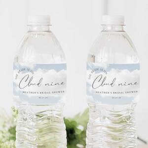 May include: Two clear plastic water bottles with blue and white labels that say "The bride is on cloud nine" and "Heather's Bridal Shower" with the date 05.27.24.