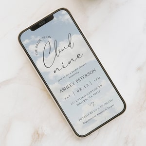 May include: A smartphone screen displaying a bridal shower invitation with a blue sky and clouds background. The text reads "The bride is on cloud nine" and includes the bride's name, date, time, and location. The invitation also includes information about the registry.