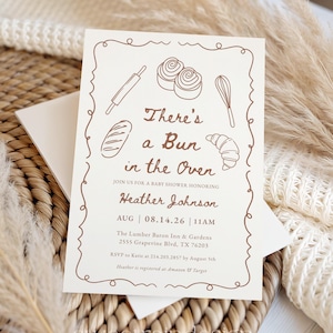 Può includere: Invito per baby shower color crema con disegni a tratto marrone di utensili da forno e pasticcini. Il testo recita "There's a Bun in the Oven" e invita gli ospiti a celebrare Heather Johnson. Include data, ora e luogo.