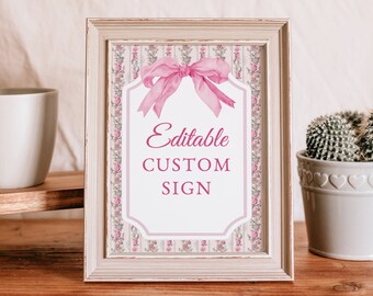 Peut inclure: Un panneau encadré avec le texte "Editable CUSTOM SIGN" en rose. Le panneau a un nœud rose et une bordure florale. Le cadre est blanc vieilli, et le panneau est affiché sur une surface en bois.