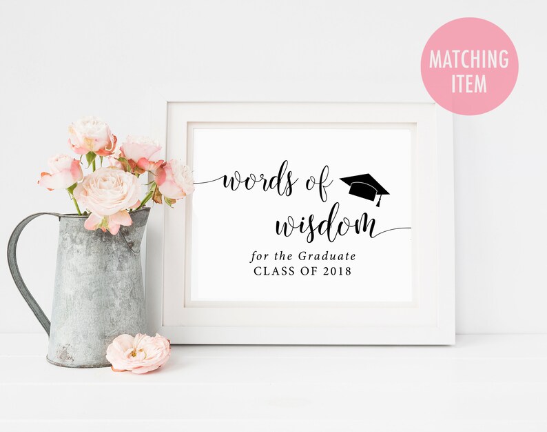 May include: White frame with a black and white sign that says "words of wisdom for the graduate class of 2018". A graduation cap is above the words. The sign is on a white surface with a bouquet of pink roses in a metal pitcher.