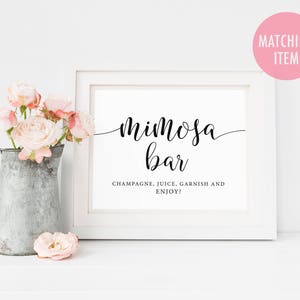 May include: White sign with black text that reads "Mimosa Bar" and "Champagne, Juice, Garnish and Enjoy!"  The sign is sitting on a white surface with a pitcher of flowers in front of it.