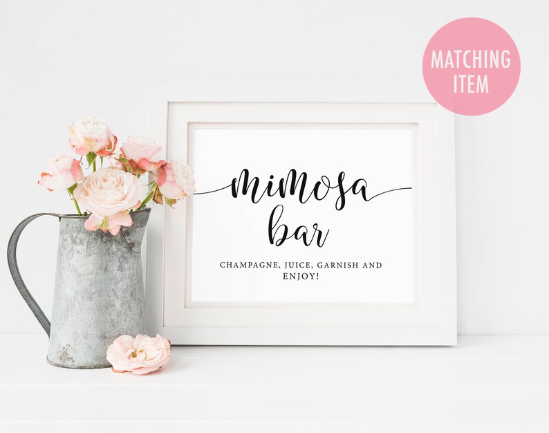 May include: White sign with black text that reads "Mimosa Bar" and "Champagne, Juice, Garnish and Enjoy!"  The sign is sitting on a white surface with a pitcher of flowers in front of it.