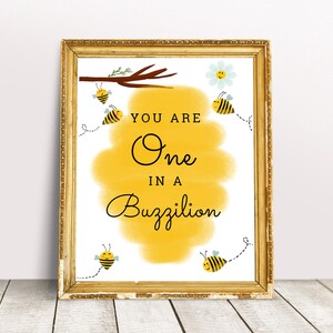 May include: A yellow and white printable sign with the text "You are One in a Buzzilion" and cartoon bees. The sign is framed in a gold frame.