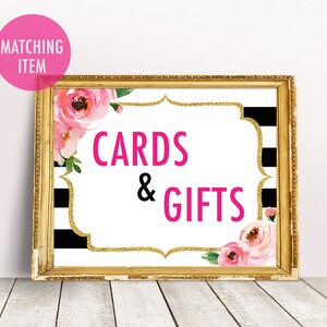 May include: A gold framed sign with black and white stripes and pink flowers. The sign says "Cards & Gifts" in pink letters.